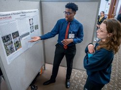 Richard Steiner-Otoo gestures while discussing his research poster at a symposium.