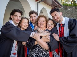 The Povolo quintuplets in graduation gowns surround and hug a smiling woman.
