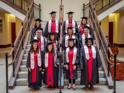 A group of 12 graduates stand on a staircase.