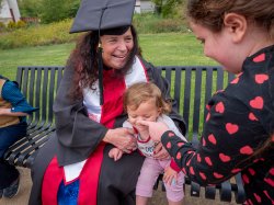 A grandmother in a cap and gown plays with her grandbaby and older grandchild.