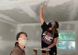 Mariana Luna-Martinez paints a ceiling while standing on a ladder.