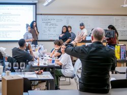 Godek listens to discussion about tasting wines in a college classroom. Adjunct Professor Stephen Fahy is speaking to students with his back toward the camera.(Photo by University Photographer Mike Peters)