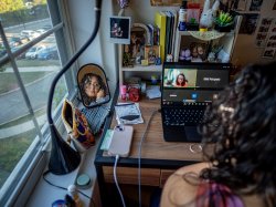 Sara Flores sits at her desk during a Zoom meeting on her laptop. Her reflection appears in a small mirror beside her.