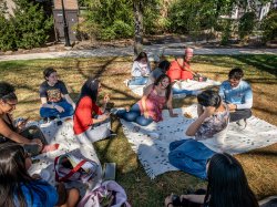 Sara Flores talks with a group of students sitting on blankets on campus.