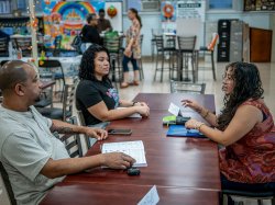 Sara Flores sits facing two adults in a classroom at Eastside High School, assisting them with English as part of the community-focused language program.