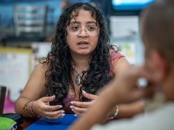 Sara Flores gestures with her hands while seated at a table.