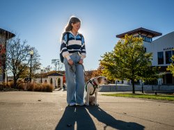 Makayla Snyder walks on campus with Katherine, her young yellow Labrador retriever in training, who wears a green “Seeing Eye Puppy” vest.