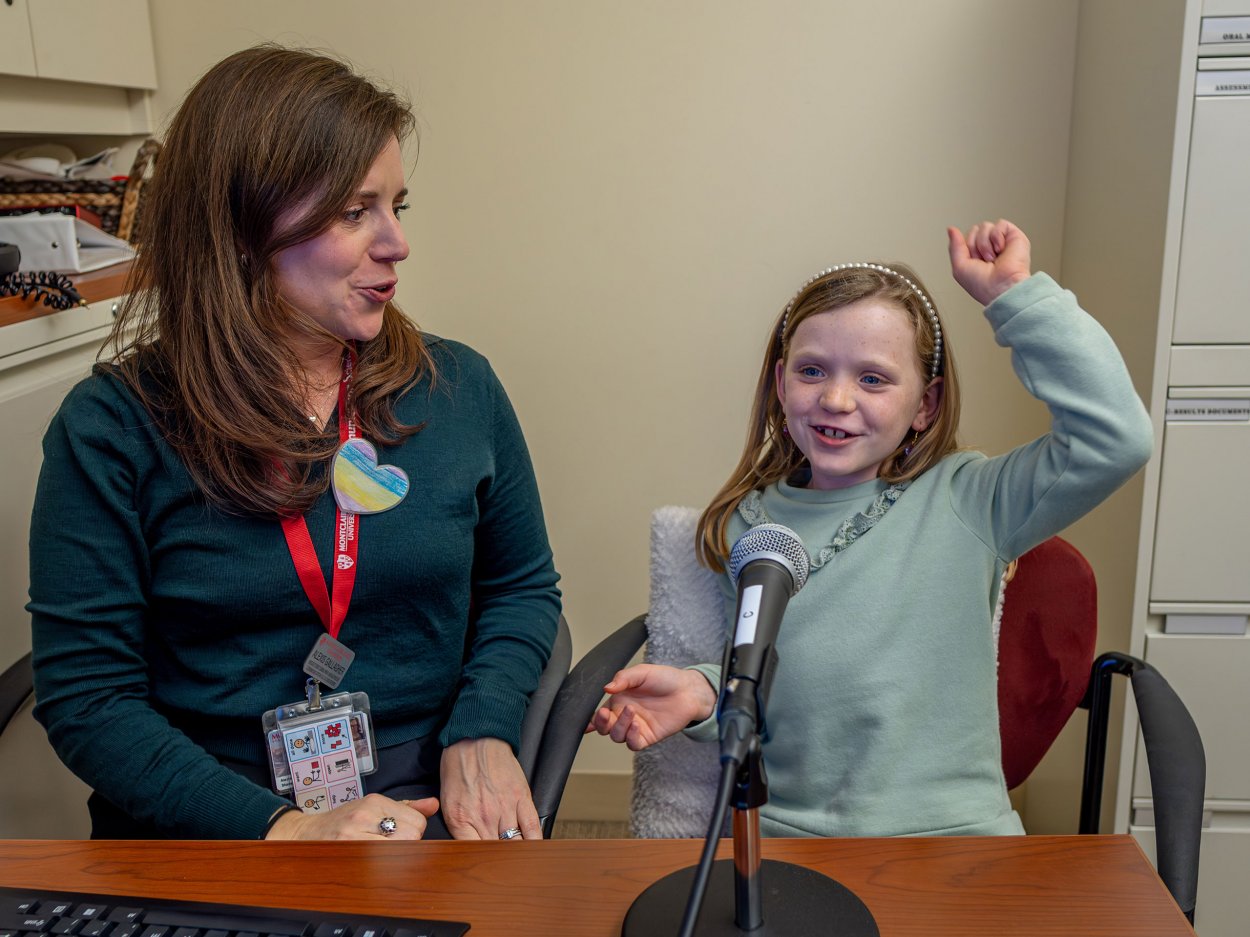 Colette raises an arm in celebration during her speech therapy session under the guidance of Alexis Gallagher.