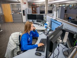 Olga Mikutina answers the phone in front of computer screens at the IT Service Desk.