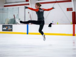 Olga Mikutina, wearing “Olympic Team Austria” jacket, performs a high split jump on Montclair's indoor ice rink.