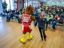 Rocky the Red Hawk mascot and handler dance in front of a large crowd of students.