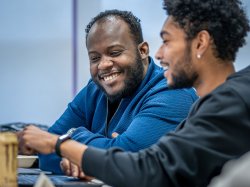 Horatio Wauchope and Gustavo Quintero sit side by side at a table in a classroom.