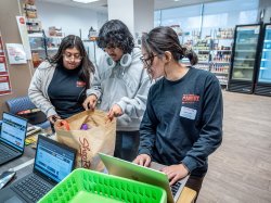 Monica Morales and Mahir Ahmed weigh a bag of food, while Kaori Sakae logs it into her computer.