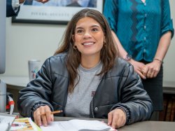 Transfer student Abigail Rodriguez sits at a desk inside a classroom with a notebook in front of her and holding a pencil.