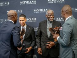 Trailblazer Award honorees Tommy Foster and Professor Leslie Wilson stand with Montclair leaders during the MEGA Symposium, talking in front of a Montclair State University backdrop.