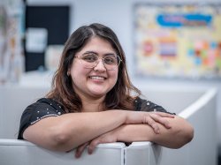 Isabella Zarate Gonzalez leans on a white cubicle wall with arms crossed.
