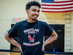 Bryce Antoine stands in a gym wearing a Montclair State Cheerleading T‑shirt, hands on hips, representing his role on the Montclair State University Coed Cheer Team.