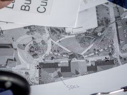 Close‑up of a printed aerial map of campus covered with hand‑drawn circles, numbers and arrows, showing Casey’s scribbled notes and table placements for the World’s Fair Day event layout.