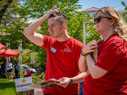 Casey Coleman and a student, Hannah Minor, stand side by side on the lawn, both holding clipboards as they look ahead thoughtfully, conferring about a checklist.