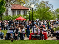 Large crowds of students, families and children fill campus, weaving between rows of red‑topped booths, game tables and food lines.
