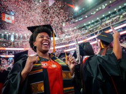 Graduate in cap and gown cheering as red and white confetti fills the air during Montclair State University’s 2026 Spring Commencement at Prudential Center.