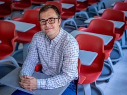 Jacob Roby sits in a classroom full of red chairs.