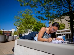A student writes in a notebook outdoors.