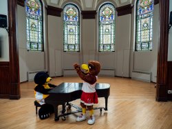 Ethan Garcia plays piano dressed as Deacon the Bear as Rocky the Redhawk applauds.