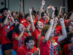 Close-up of students in red Montclair State EOF T-shirts raising their arms and cheering with their mouths open in excitement.