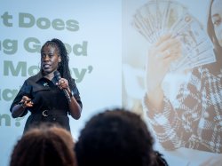 Keynote speaker Tiffany 'The Budgetnista' Aliche speaks into a microphone on stage, with an image of a hand holding cash projected on the screen behind her.