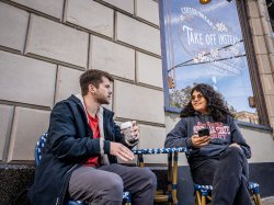Two students chat while sitting at a coffee shop’s outdoor table.