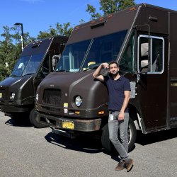 Kaan Esendemir standing in front of two delivery trucks.