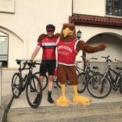 Professor Andrew Scanlon posing with Rocky the Red Hawk outside of the School of Nursing