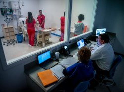 Nursing professor and faculty observing students in simulation lab.