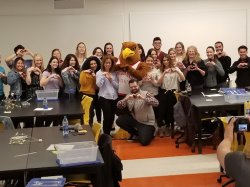 Team Red Hawk (consisting of faculty, staff, and students) posing with Rocky the Red Hawk in a classroom.