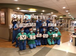 Nurses in scrubs holding signs that spell out 'Strong Than the Virus'.
