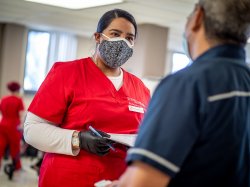 Nursing student wearing protective face mask and gloves speaking to an out of focus patient.