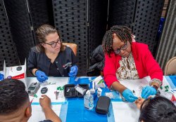 School of Nursing alumni and professor taking a fingerstick sample during a health screening.