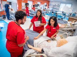 students wearing red scrubs gathered around a mannequinn on a medical bed