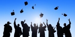 photo includes dark silhouettes of students throwing graduation caps in the air with blue sky background