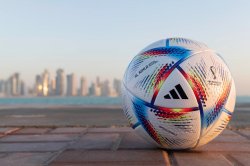 A colorful soccer ball with a brand logo in the foreground with a Qatar skyline of in the background