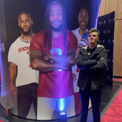 Student smiling and standing in front of large cardboard cutouts of three football players.