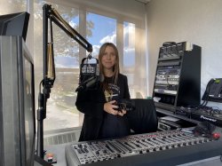 A woman standing in front of a radio control mixer and microphone.