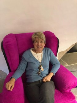 A smiling woman sitting in a purple chair looking up and straight ahead
