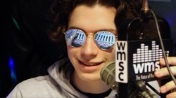 A closeup of a male college student wearing sunglasses next to a radio microphone.
