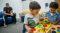 Image of children in a clinicial setting playing with blocks while parent looks on.