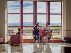 students sitting at a high-top table in open atrium. wall of windows with NYC skyline is in the background