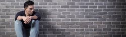 Young person sitting alone against a brick wall