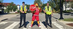 Picture of the Red the Red Hawk with two University Police Officers on a campus crosswalk.