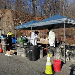 Photo of the staff from SCS Engineers as they stand around a sorting table performing a waste audit. They are dressed in personal protective equipment and surrounded by empty waste bins to collect the various types of waste they sort out.